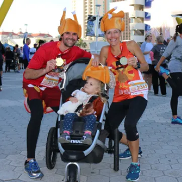 a man and woman pose with child in stroller at Tampa YMCA turkey gobble race, all wearing turkey hats